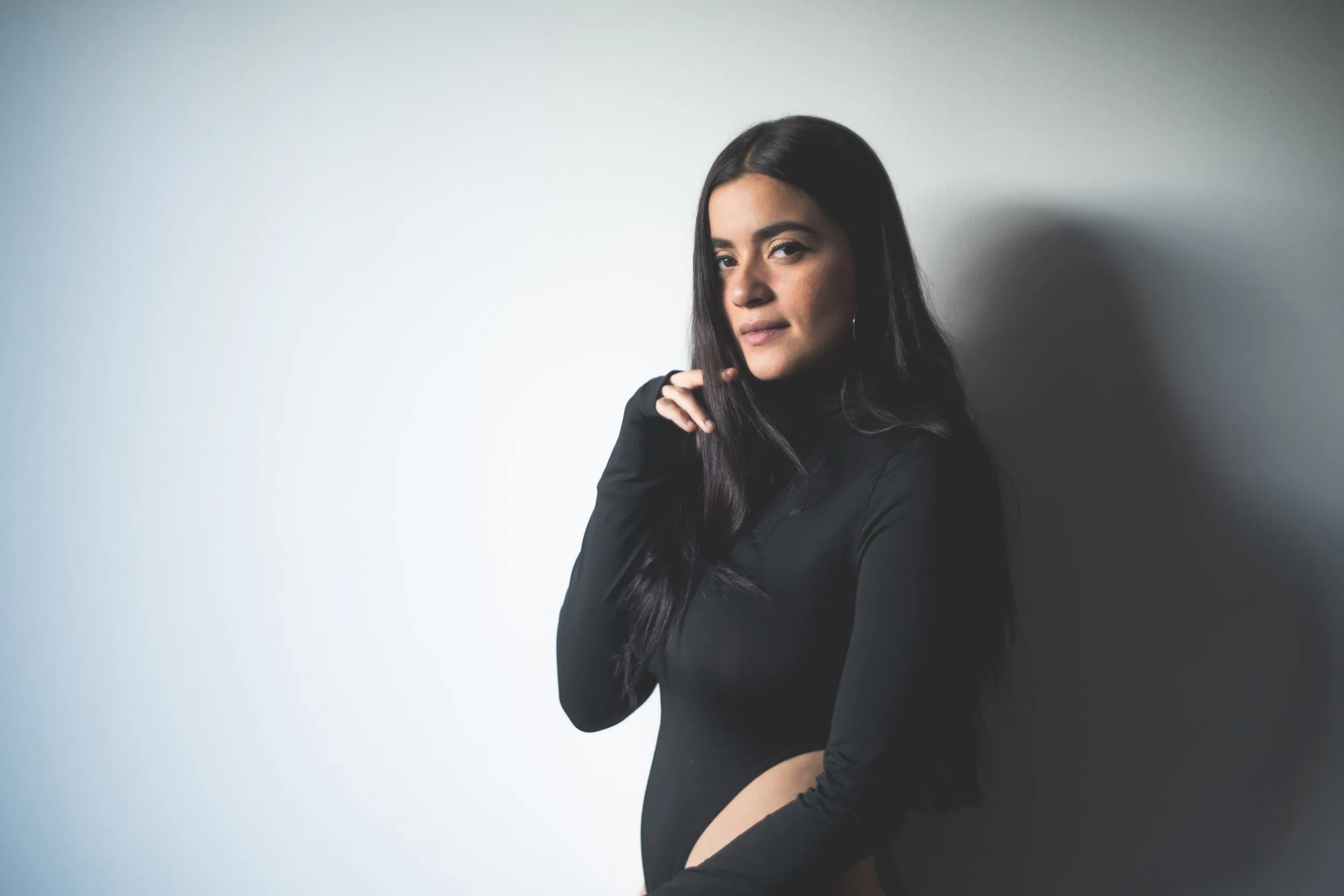 Paulina Gaitán de pie junto a una pared blanca, con suéter negro de cuello alto