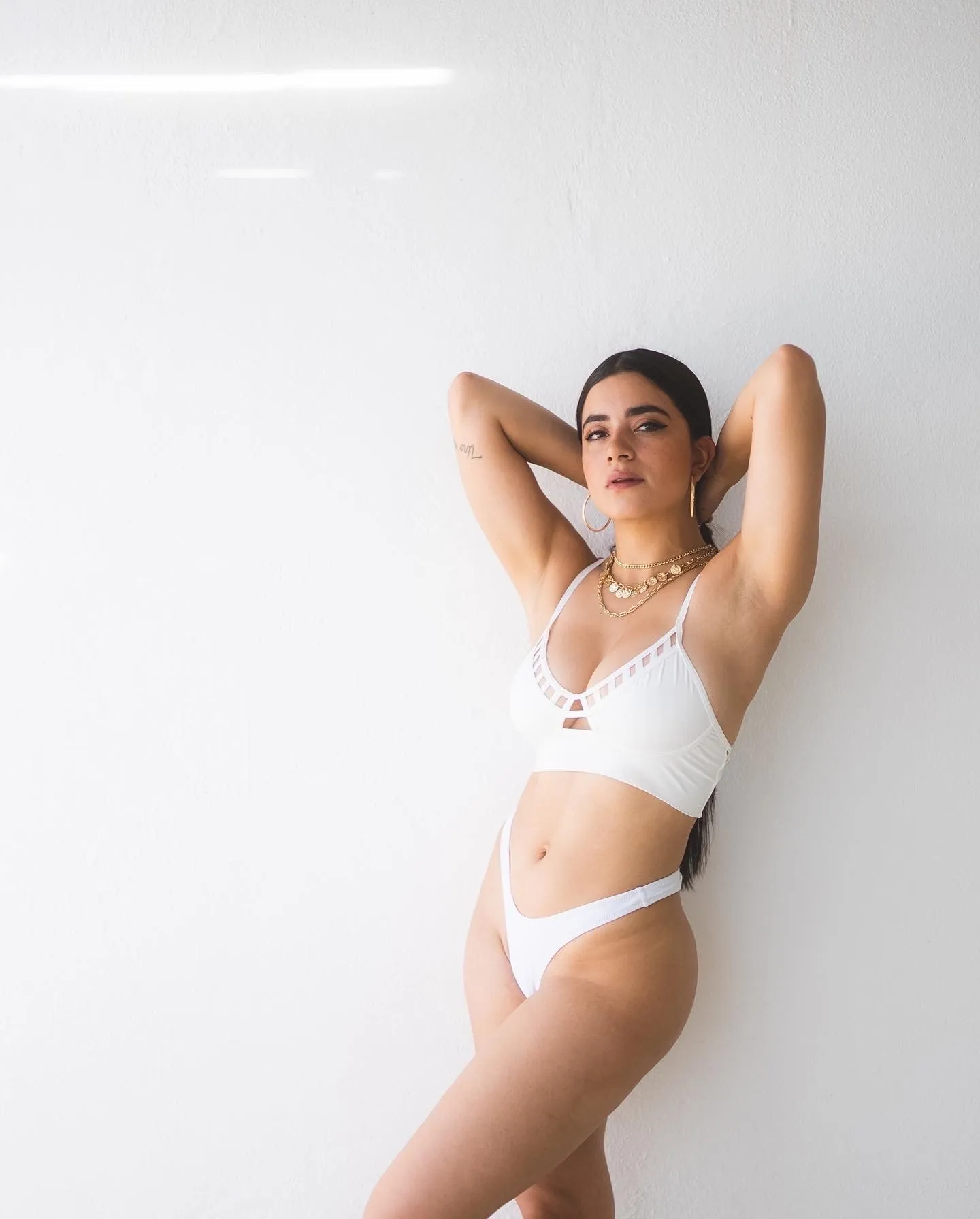Paulina Gaitán recostada sobre un fondo rosa con traje de baño blanco